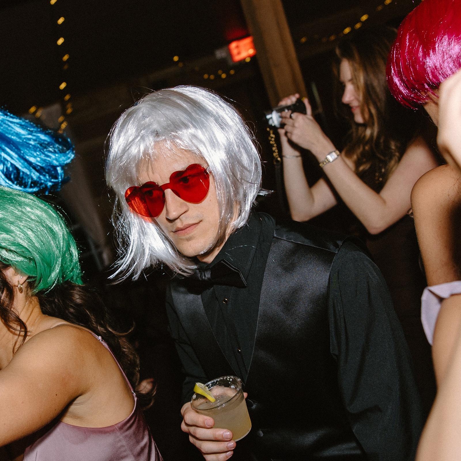 Ben Sledge in a silver wig and red heart-shaped sunglasses at an event.